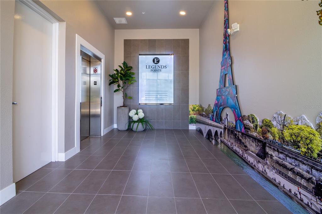 A modern apartment building lobby features a tiled floor, an elevator, and a mural wall — 4290 S HIGHWAY 27 UNIT 206, CLERMONT, FL