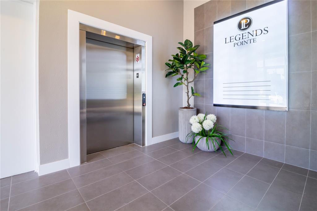 An elevator lobby features gray tiled floors, a metallic elevator, and a decorative wall sign — 4290 S HIGHWAY 27 UNIT 206, CLERMONT, FL