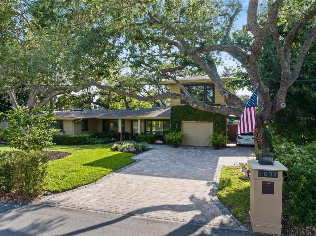 A two-story house with a paved driveway, large oak trees, and an American flag — 1827 BAYWOOD DRIVE, SARASOTA, FL