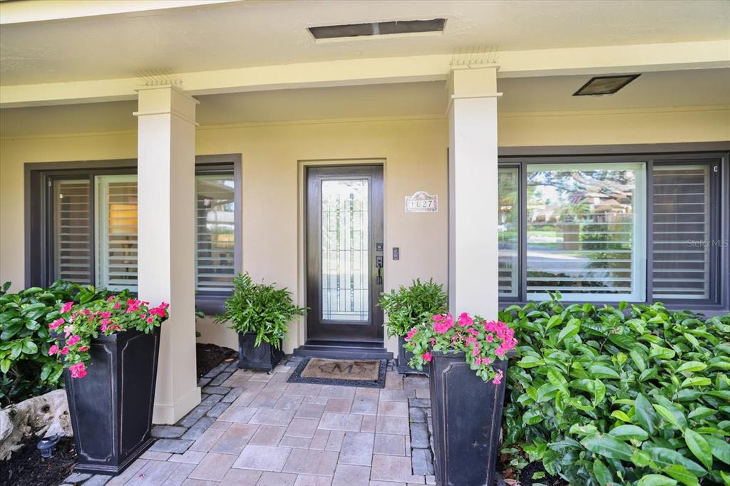 A paved walkway leads to a front door flanked by two large planters with flowers — 1827 BAYWOOD DRIVE, SARASOTA, FL