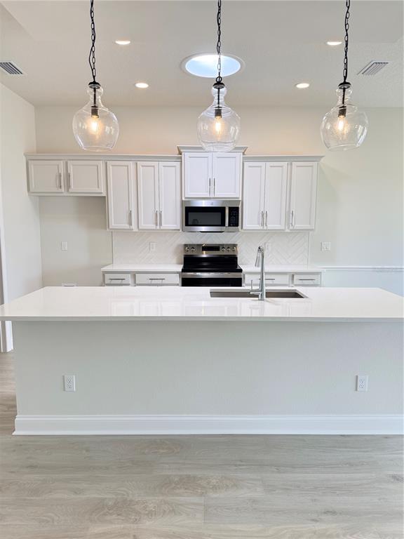 A kitchen features white cabinets, a large island with a sink, and three glass pendants — 29 SPRING STREET, PALM COAST, FL