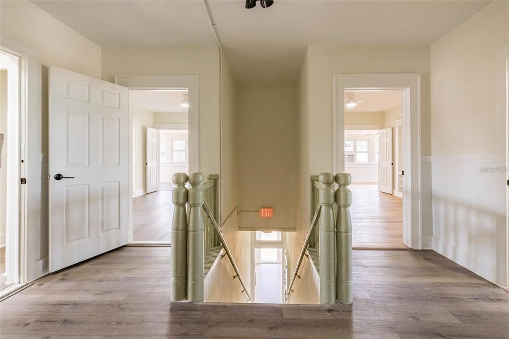 A hallway with light wood flooring features a central staircase and two open doorways — 218 N PINELLAS AVENUE, TARPON SPRINGS, FL