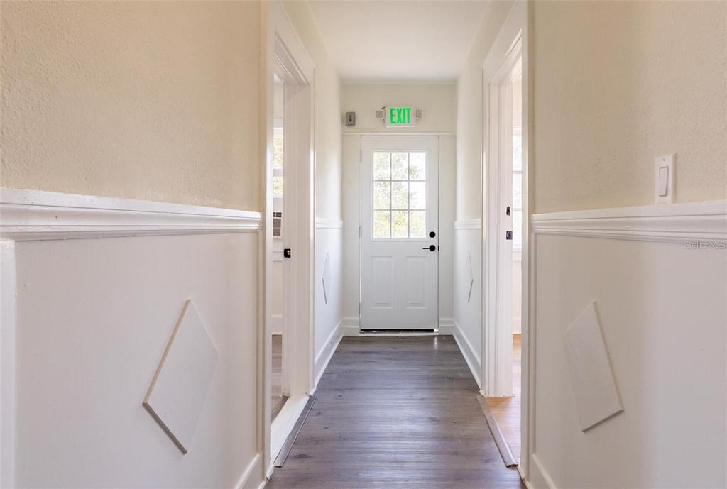 A hallway with wood-look flooring, white wainscoting, and a white door with an exit sign — 218 N PINELLAS AVENUE, TARPON SPRINGS, FL