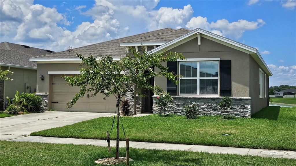 A single-story house with a tan stucco exterior, stone accents, and a two-car garage — 8103 WHEAT STONE DRIVE, ZEPHYRHILLS, FL