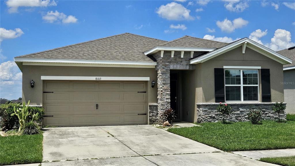 A single-story house with a tan stucco exterior, stone accents, and a two-car garage — 8103 WHEAT STONE DRIVE, ZEPHYRHILLS, FL