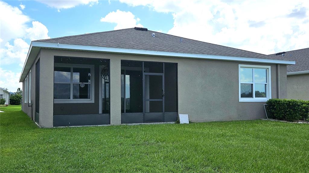 The exterior rear view of a house features a screened-in patio and a grassy lawn — 8103 WHEAT STONE DRIVE, ZEPHYRHILLS, FL