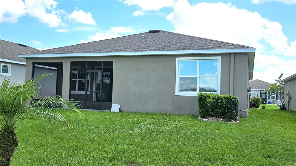 The exterior rear view of a single-story house features a screened-in lanai and lawn — 8103 WHEAT STONE DRIVE, ZEPHYRHILLS, FL