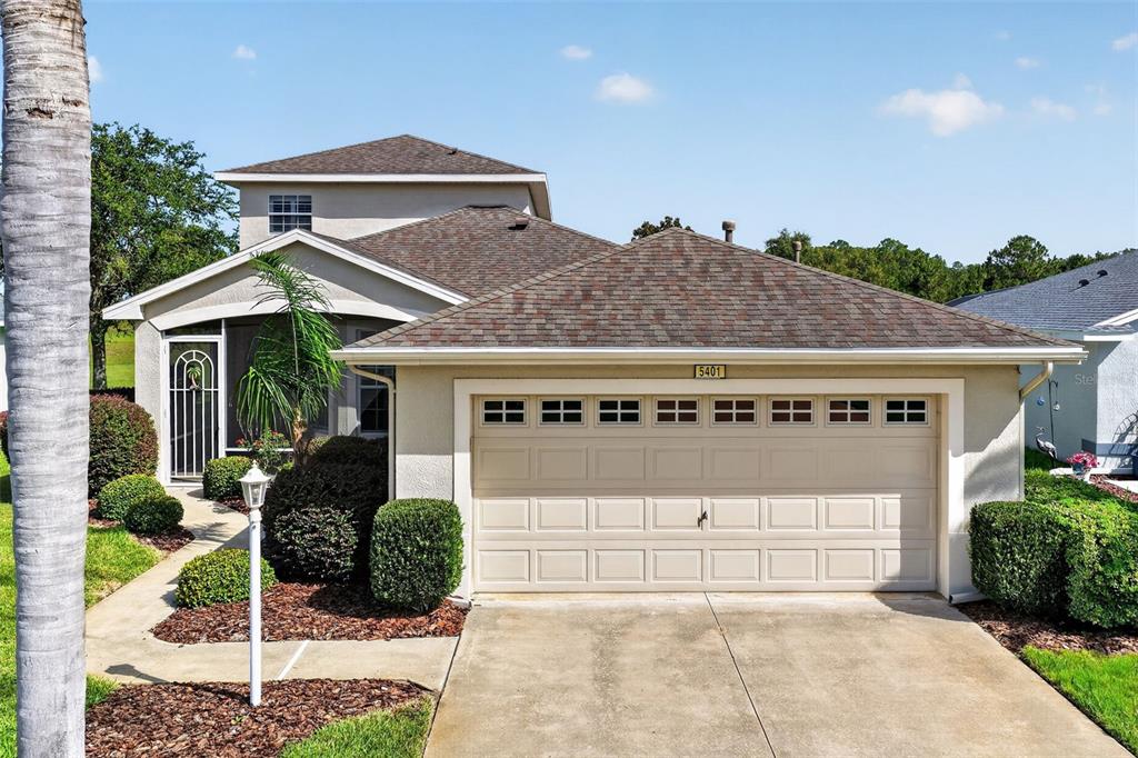 A two-story house features a beige stucco exterior, a two-car garage, and landscaped front bushes — 5401 SIR CHURCHILL DRIVE, LEESBURG, FL