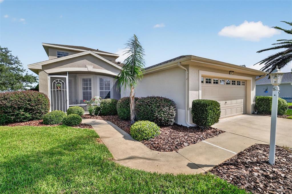 A single-story house with a screened front porch, a two-car garage, and landscaped front yard — 5401 SIR CHURCHILL DRIVE, LEESBURG, FL