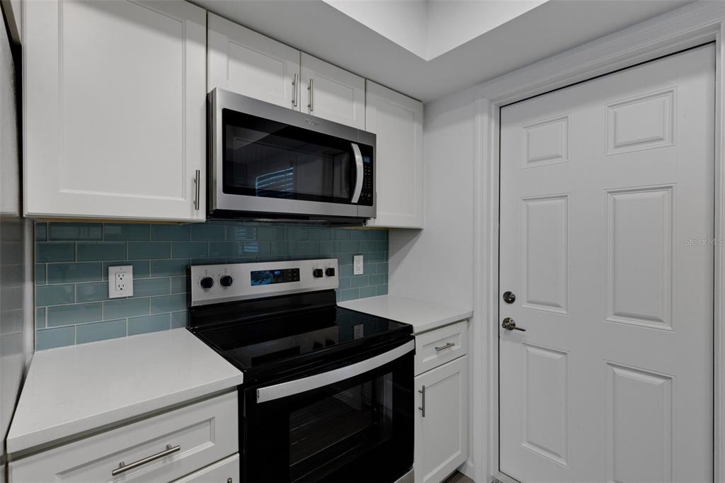 A kitchen features white cabinets, a stainless steel microwave, a black stove, and blue backsplash — 2826 W RAINBOW CIRCLE UNIT 2818, SARASOTA, FL