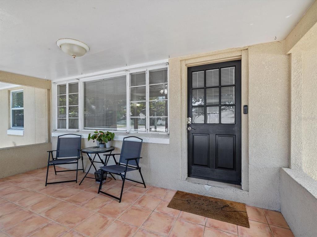 A covered porch features tiled flooring, a black front door, and a small bistro set — 5015 15TH AVENUE S, GULFPORT, FL