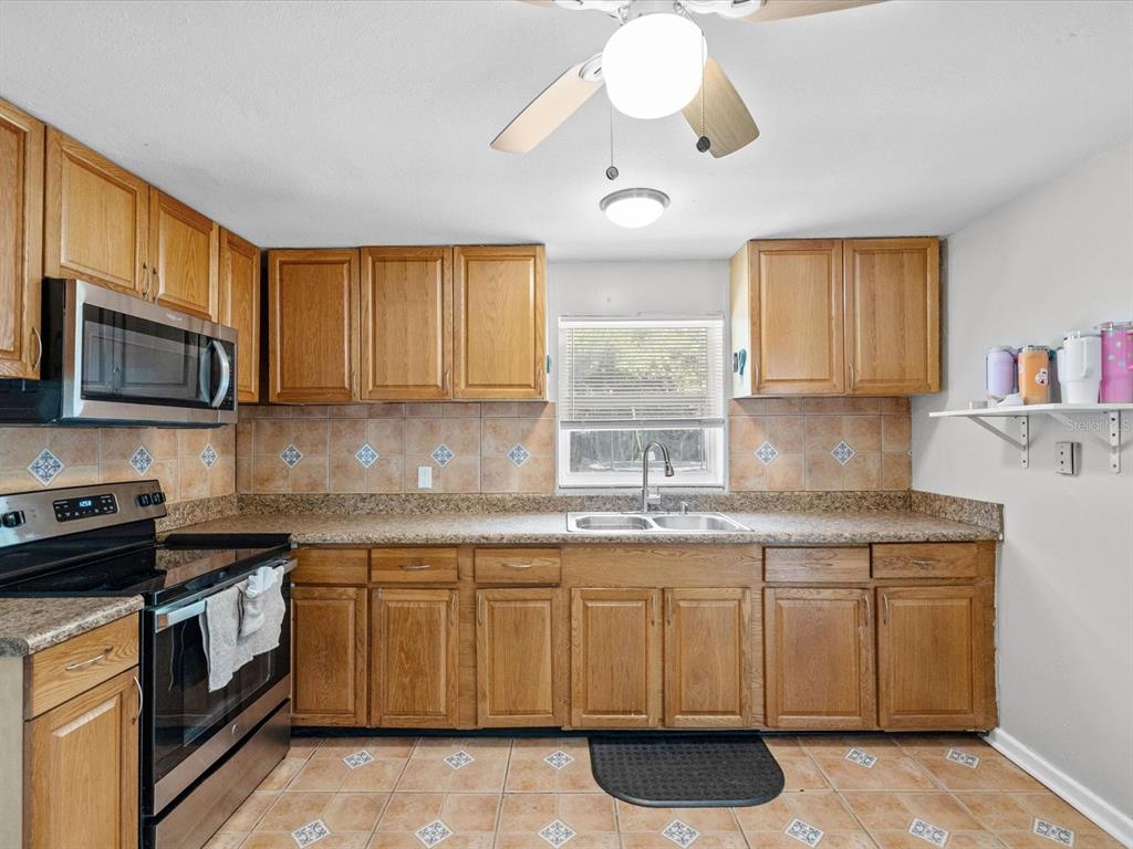 A kitchen with oak cabinets, stainless steel appliances, tile backsplash, and a double sink — 5015 15TH AVENUE S, GULFPORT, FL