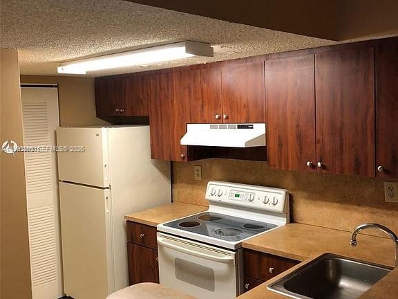 A kitchen features dark wood cabinets, a white refrigerator, a white stove, and laminate countertops — 7235 NW 179th St # 103, Hialeah FL 33015, HIALEAH, FL