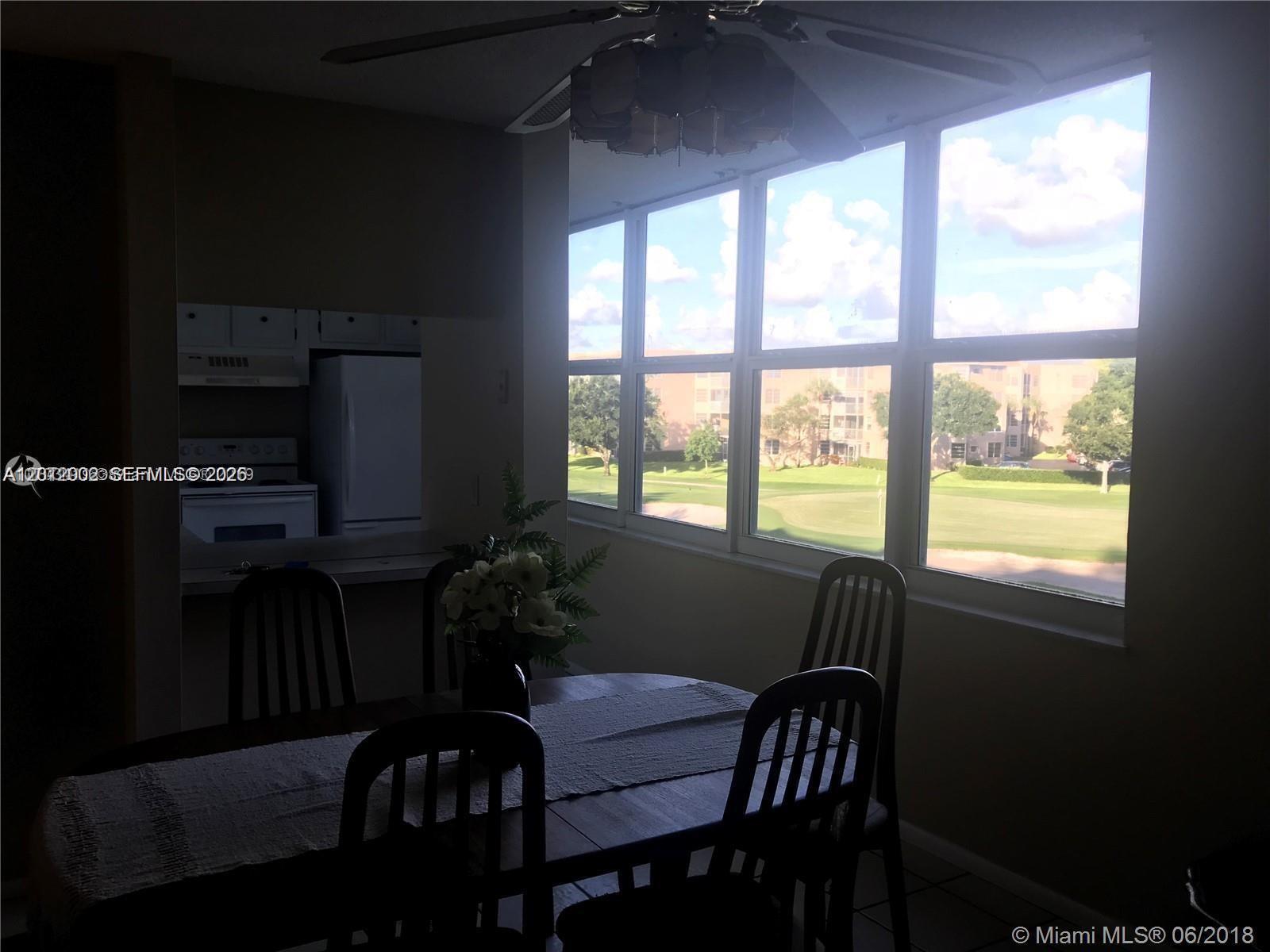 A dining area features a wooden table and chairs overlooking a golf course through windows — 9470 Live Oak Pl # 306, Davie FL 33324, DAVIE, FL