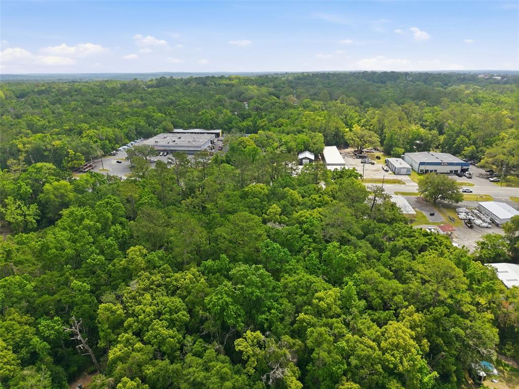 An aerial view shows a large wooded area adjacent to several commercial warehouse buildings — PONCE DE LEON BOULEVARD, BROOKSVILLE, FL