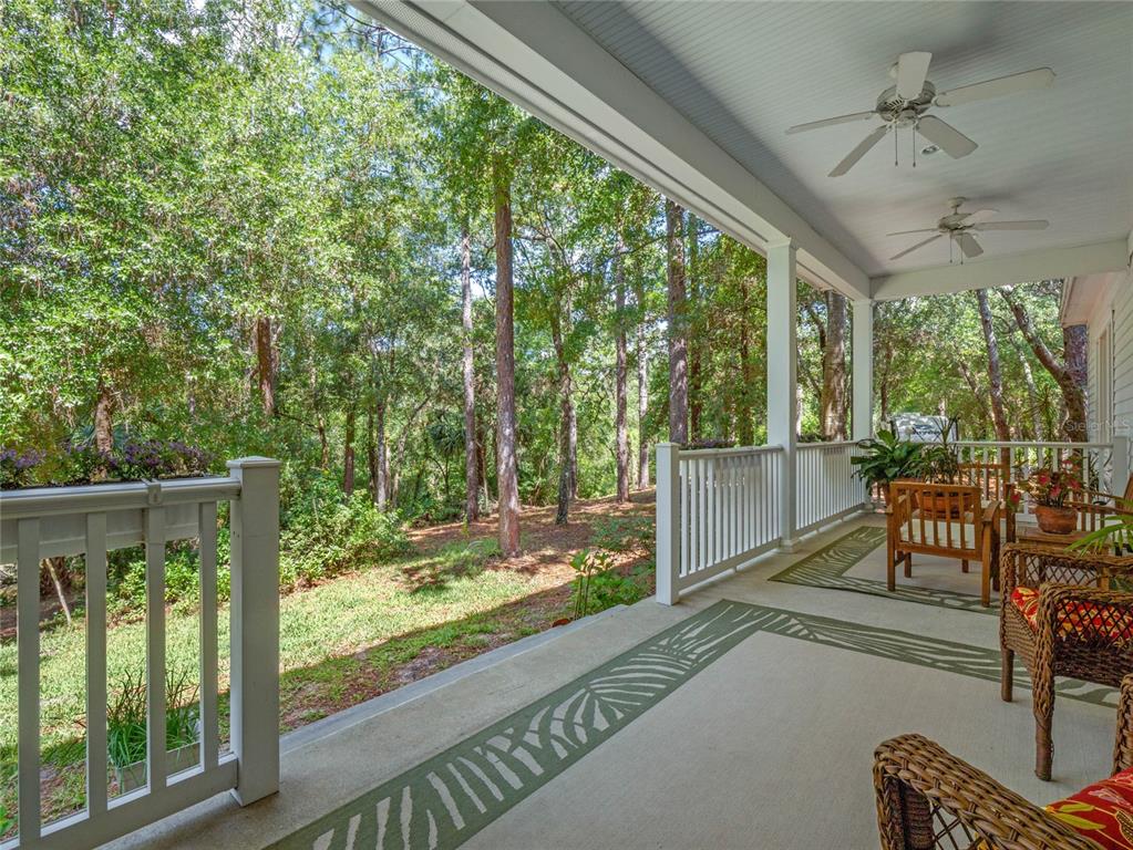 A covered porch with ceiling fans overlooks a wooded backyard with a white railing — 4000 ROUSE ROAD, ORLANDO, FL