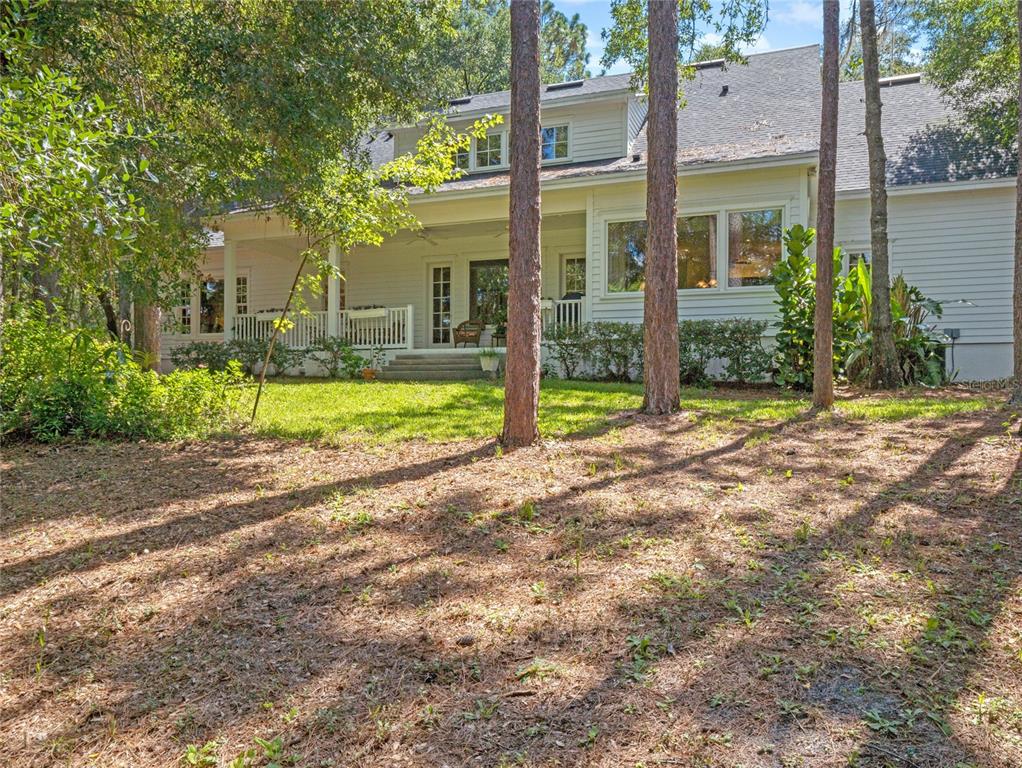 The rear exterior of a white two-story house features a covered porch and wooded yard — 4000 ROUSE ROAD, ORLANDO, FL
