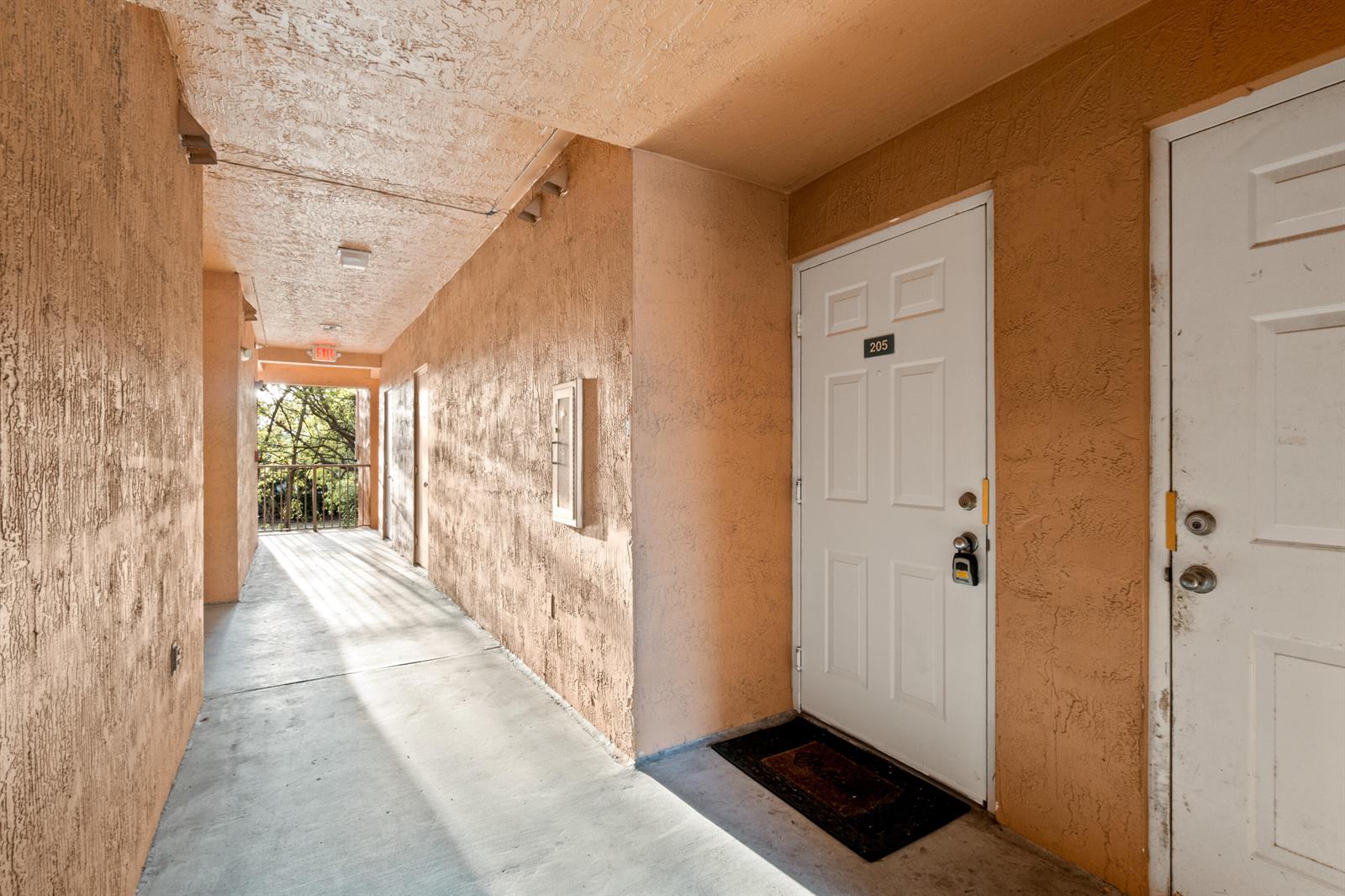 An outdoor apartment hallway with textured peach walls, concrete flooring, and two white doors — 6960 SW 39th # E205, Davie FL 33314, DAVIE, FL