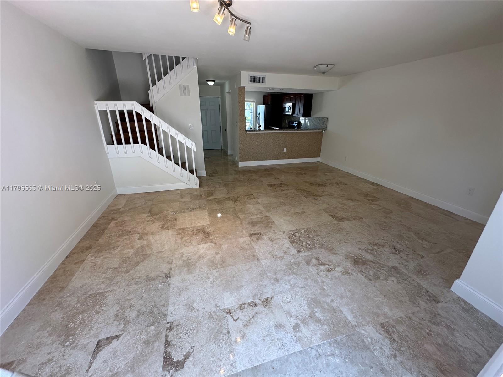 An open living area features large beige tile flooring, a white staircase, and a kitchen — 878 Crystal Lake Dr, Deerfield Beach FL 33064, DEERFIELD BEACH, FL