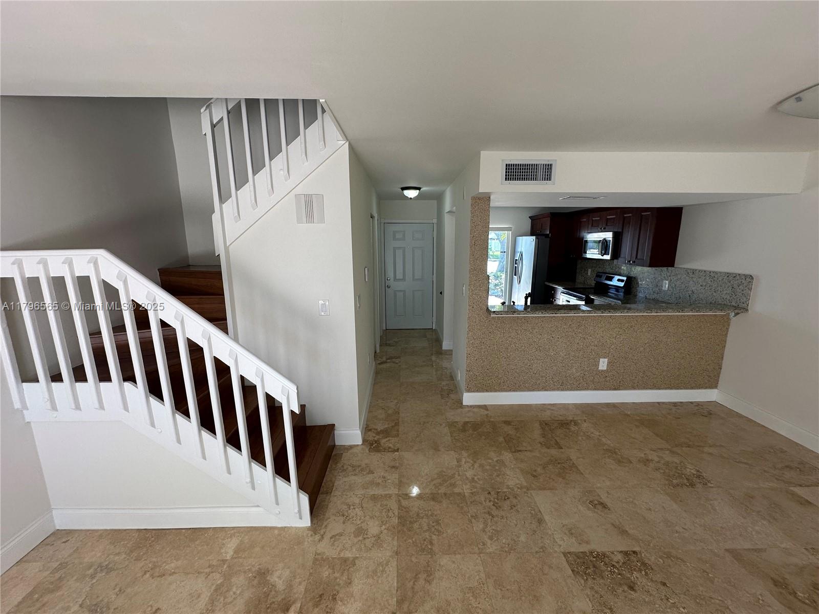 A staircase with white railings leads upward next to a kitchen with a breakfast bar — 878 Crystal Lake Dr, Deerfield Beach FL 33064, DEERFIELD BEACH, FL