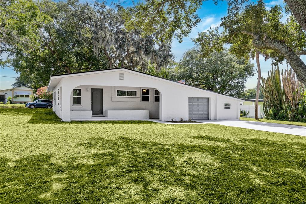 A white single-story house with a front porch, attached garage, and large surrounding trees — 1375 LAKE DRIVE, CASSELBERRY, FL