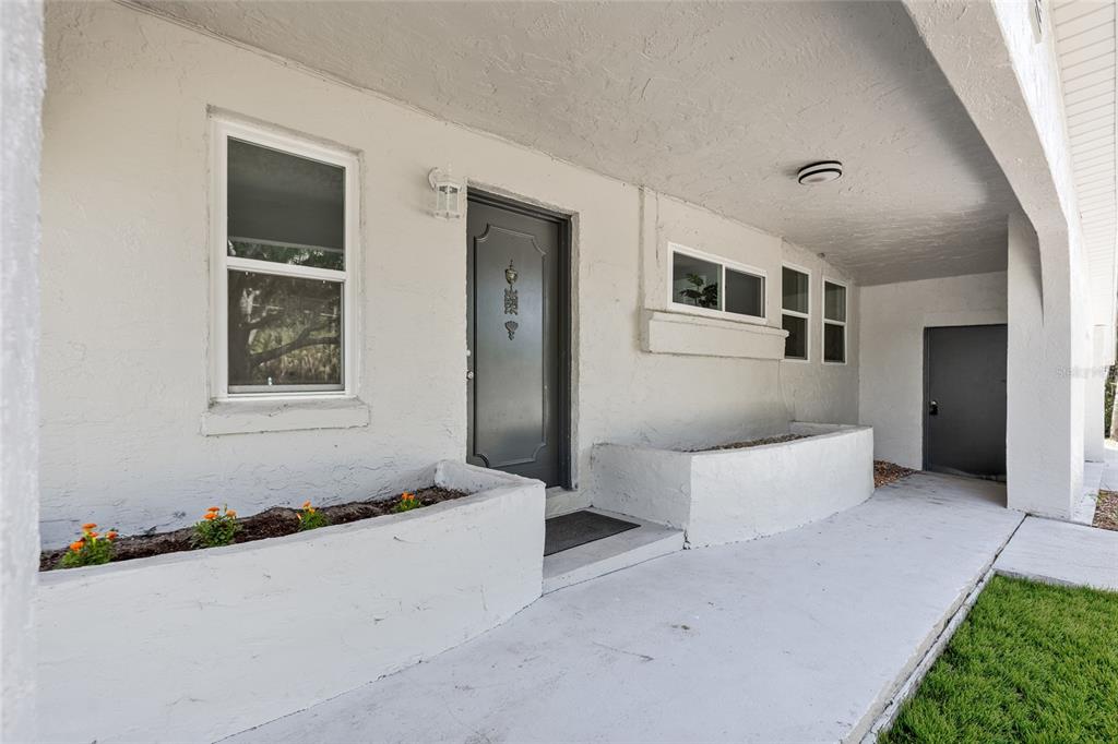 A covered concrete porch features two built-in planters, a gray front door, and a side entrance — 1375 LAKE DRIVE, CASSELBERRY, FL