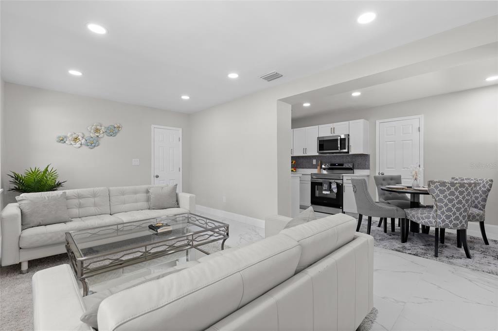 A living room with white sofas and a glass coffee table opens to a kitchen — 1375 LAKE DRIVE, CASSELBERRY, FL