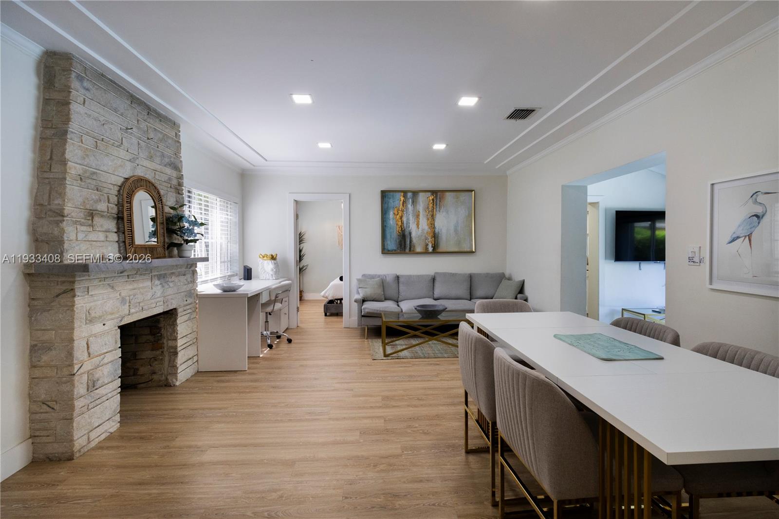This open-concept living and dining area features a stone fireplace, light wood flooring, and furniture — 437 NE 107th St, Miami FL 33161, MIAMI, FL
