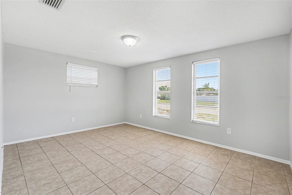 An empty room with light gray walls, tile flooring, and three windows with white blinds — 6337 BONAIRE AVENUE, NEW PORT RICHEY, FL