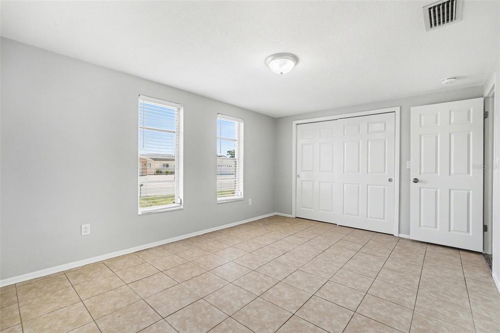 An empty bedroom features light gray walls, tile flooring, two windows, and a closet — 6337 BONAIRE AVENUE, NEW PORT RICHEY, FL