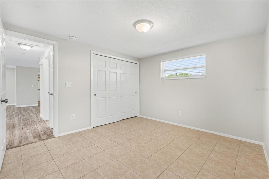 A bedroom with light-colored walls, tile flooring, a sliding closet door, and a window — 6337 BONAIRE AVENUE, NEW PORT RICHEY, FL