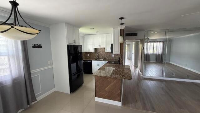 A kitchen with white cabinets, granite countertops, and a black refrigerator opens to a living area — 276 Monaco F, Delray Beach FL 33446, DELRAY BEACH, FL