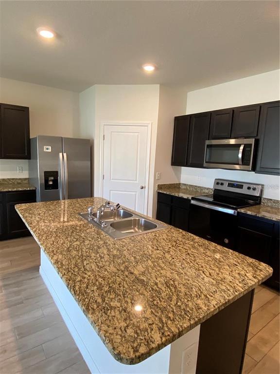A kitchen features dark cabinets, granite countertops, a central island with a sink, and appliances — 8244 SW 60TH ROAD, GAINESVILLE, FL