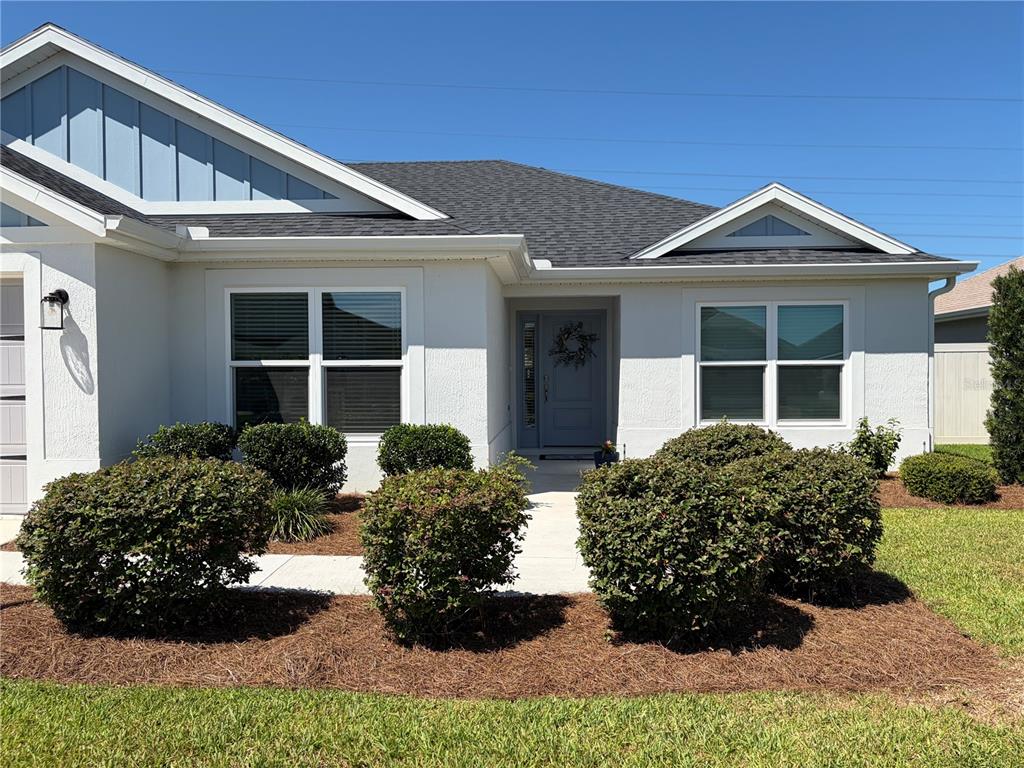 The exterior of a single-story house features white stucco walls, a gray door, and landscaping — 4540 BROOKE LANE, THE VILLAGES, FL