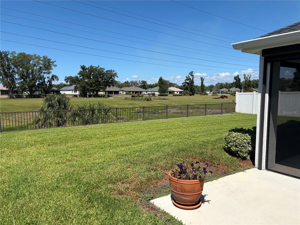 A view of a backyard with a lawn, metal fence, and a potted plant — 4540 BROOKE LANE, THE VILLAGES, FL