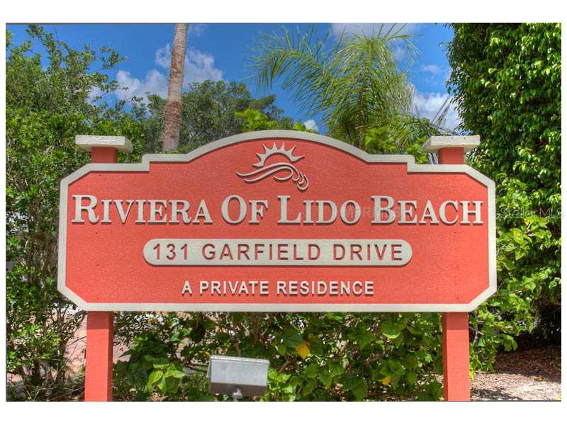 A red sign with white lettering stands outdoors surrounded by green trees and palm leaves — 131 GARFIELD DRIVE UNIT 4C, SARASOTA, FL