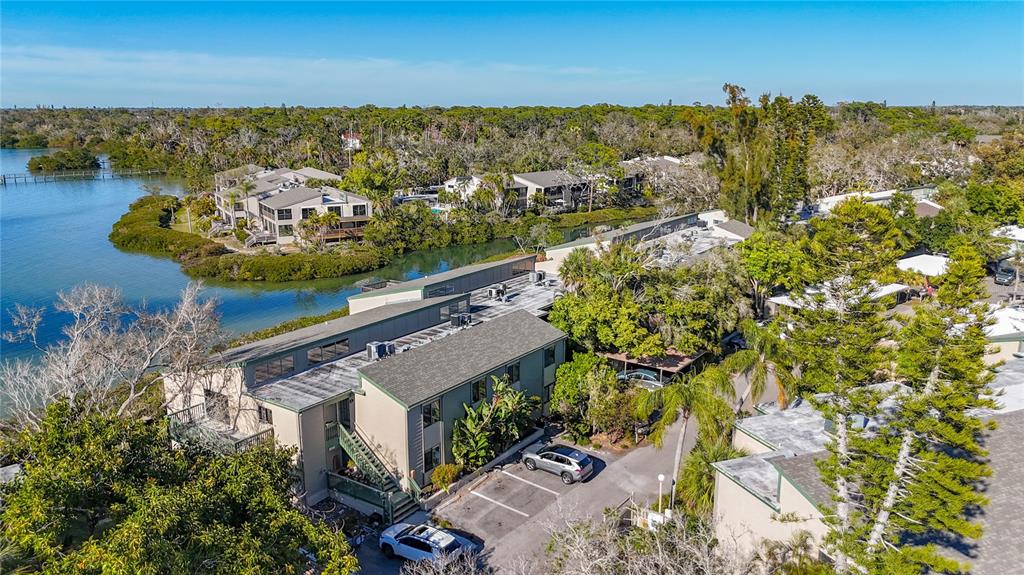 An aerial view shows multi-story apartment buildings situated near a body of water and trees — 1511 PELICAN POINT DRIVE UNIT BA180, SARASOTA, FL