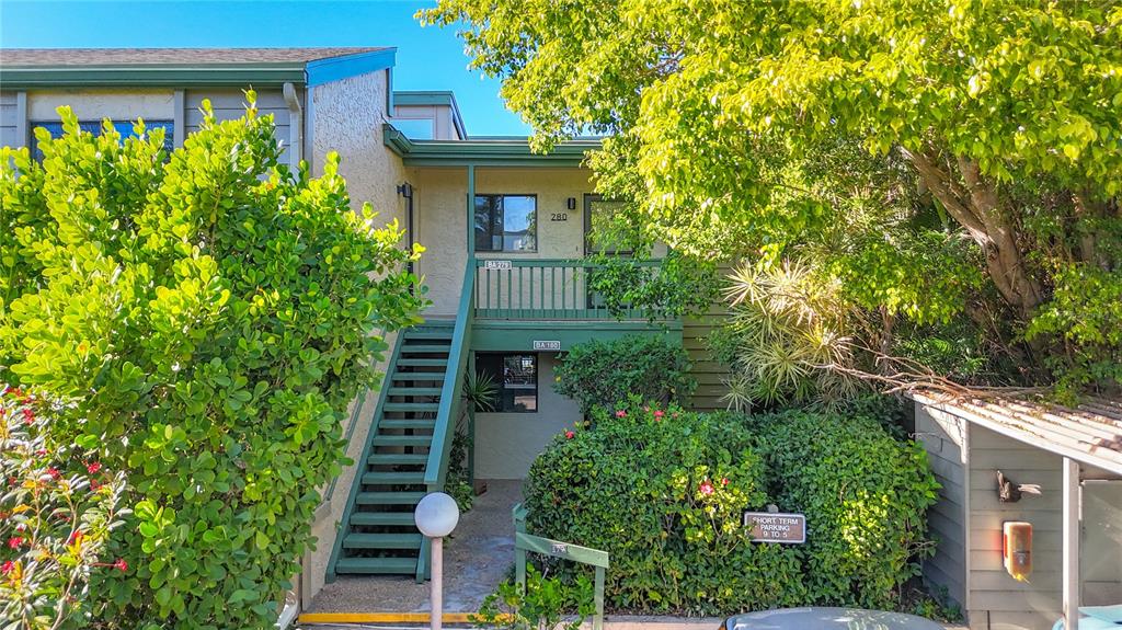 An exterior view of a two-story building with a wooden staircase leading to an upper balcony — 1511 PELICAN POINT DRIVE UNIT BA180, SARASOTA, FL