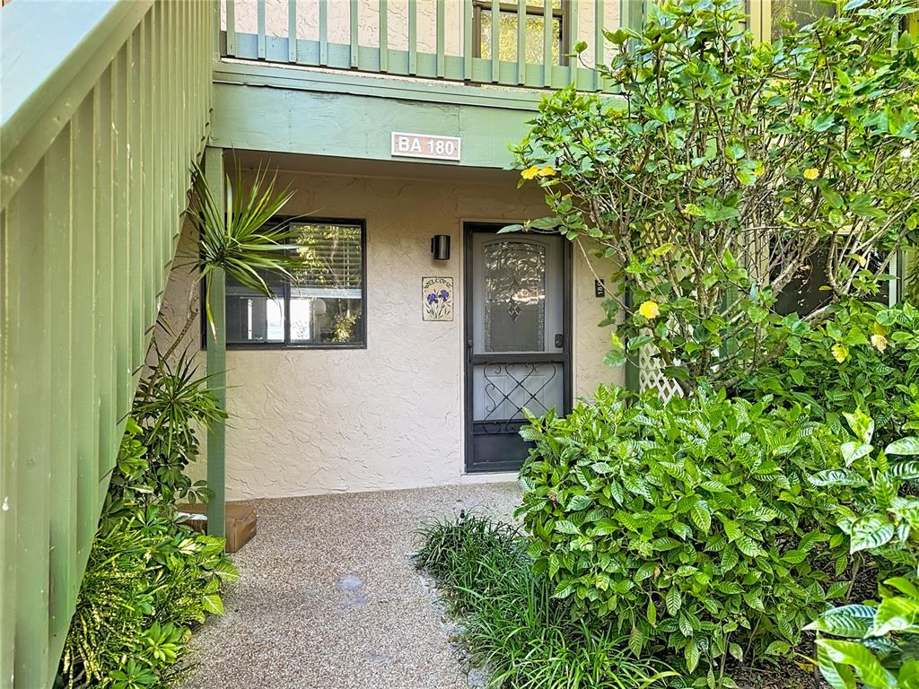 The exterior entrance of a residential unit features a green staircase, a screen door, and landscaping — 1511 PELICAN POINT DRIVE UNIT BA180, SARASOTA, FL