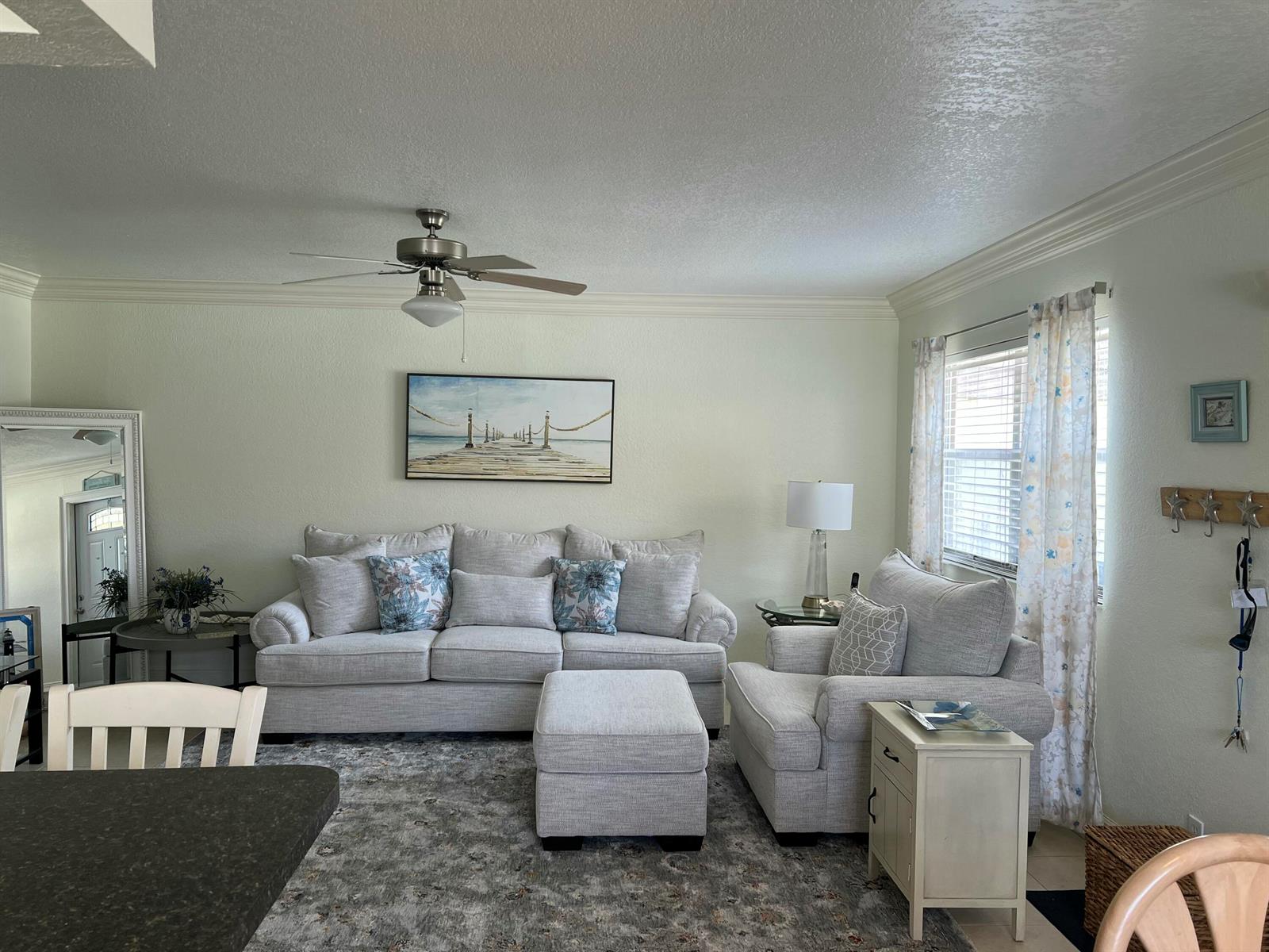 A living room features a light-colored sofa, matching armchair, ottoman, and a coastal-themed wall print — 84 Saxony B, Delray Beach FL 33446, DELRAY BEACH, FL