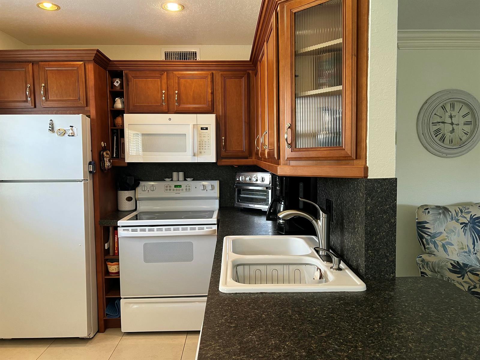 A kitchen features wood cabinets, white appliances, a double sink, and dark granite countertops — 84 Saxony B, Delray Beach FL 33446, DELRAY BEACH, FL