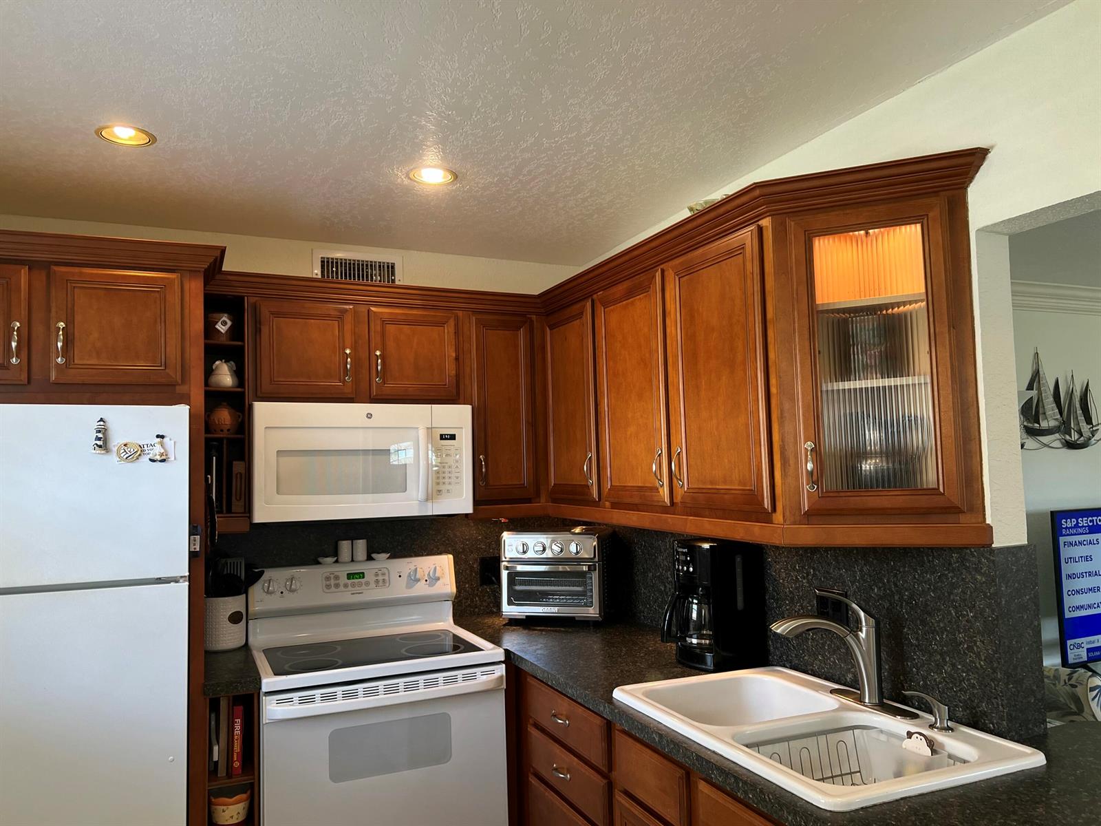 A kitchen features wood cabinets, white appliances, dark countertops, and a double-basin sink — 84 Saxony B, Delray Beach FL 33446, DELRAY BEACH, FL
