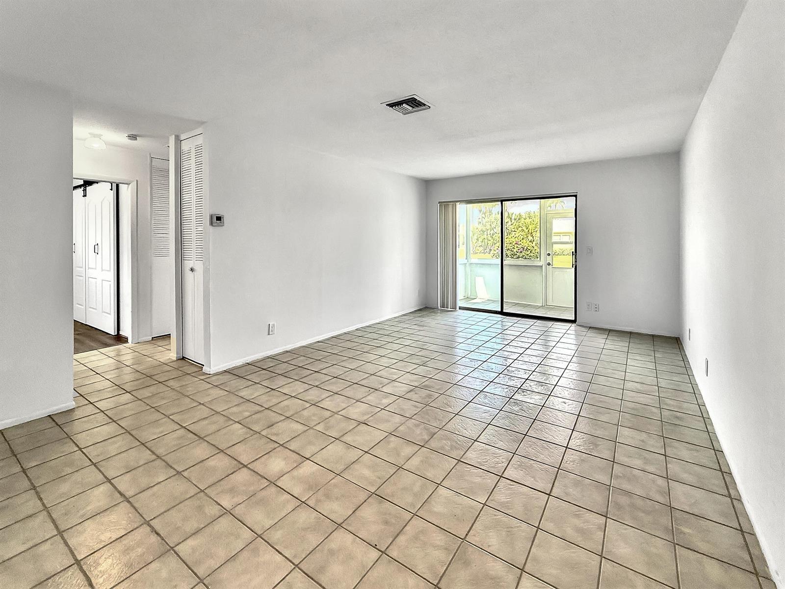 An empty living room with white walls, beige tile flooring, and a sliding glass door — 5263 Cresthaven Boulevard # A, West Palm Beach FL 33415, WEST PALM BEACH, FL