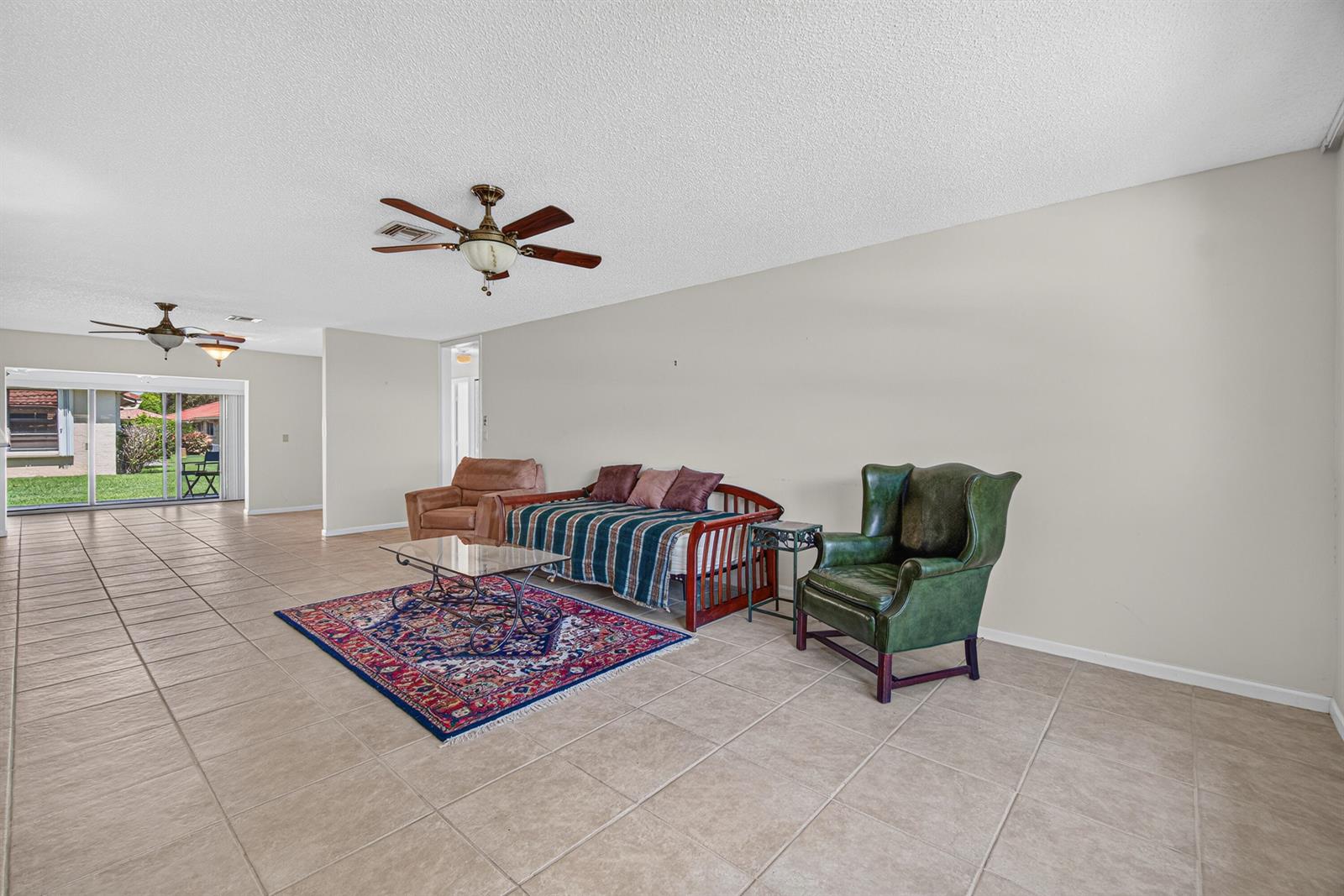 A living room with tile flooring, a daybed, a green armchair, and a patterned rug — 9925 Frangipani Tree Way # B, Boynton Beach FL 33436, BOYNTON BEACH, FL