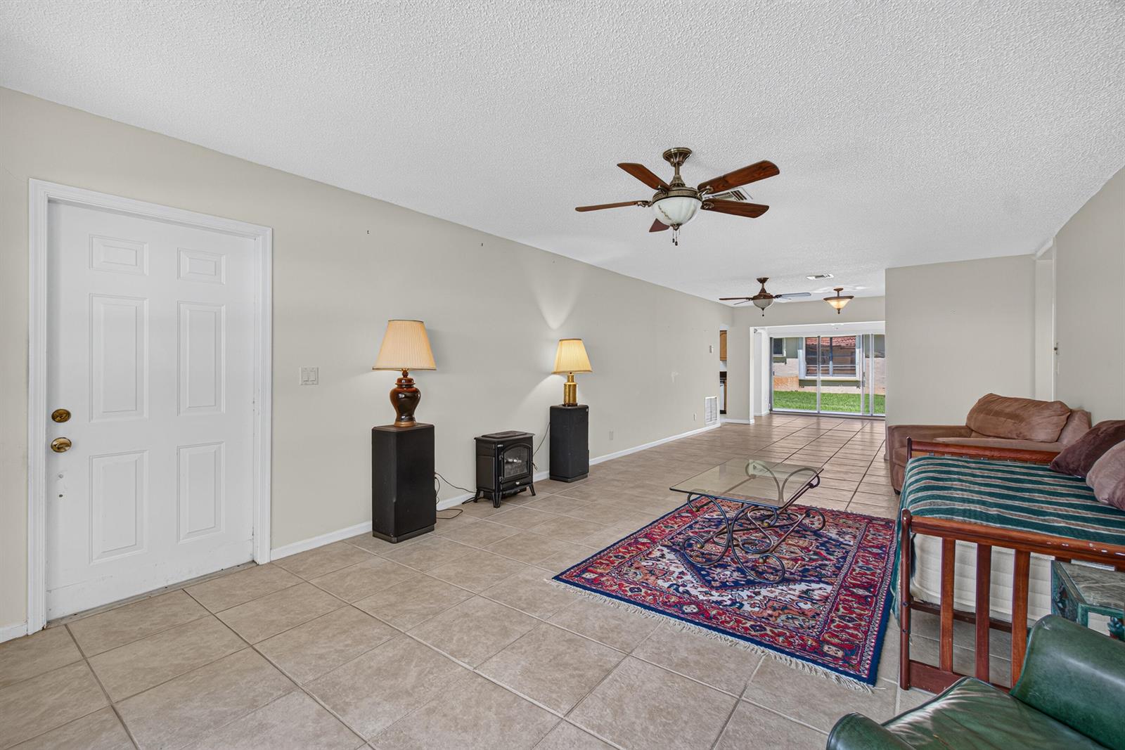 A living room features tile flooring, a ceiling fan, a rug, and a sliding glass door — 9925 Frangipani Tree Way # B, Boynton Beach FL 33436, BOYNTON BEACH, FL