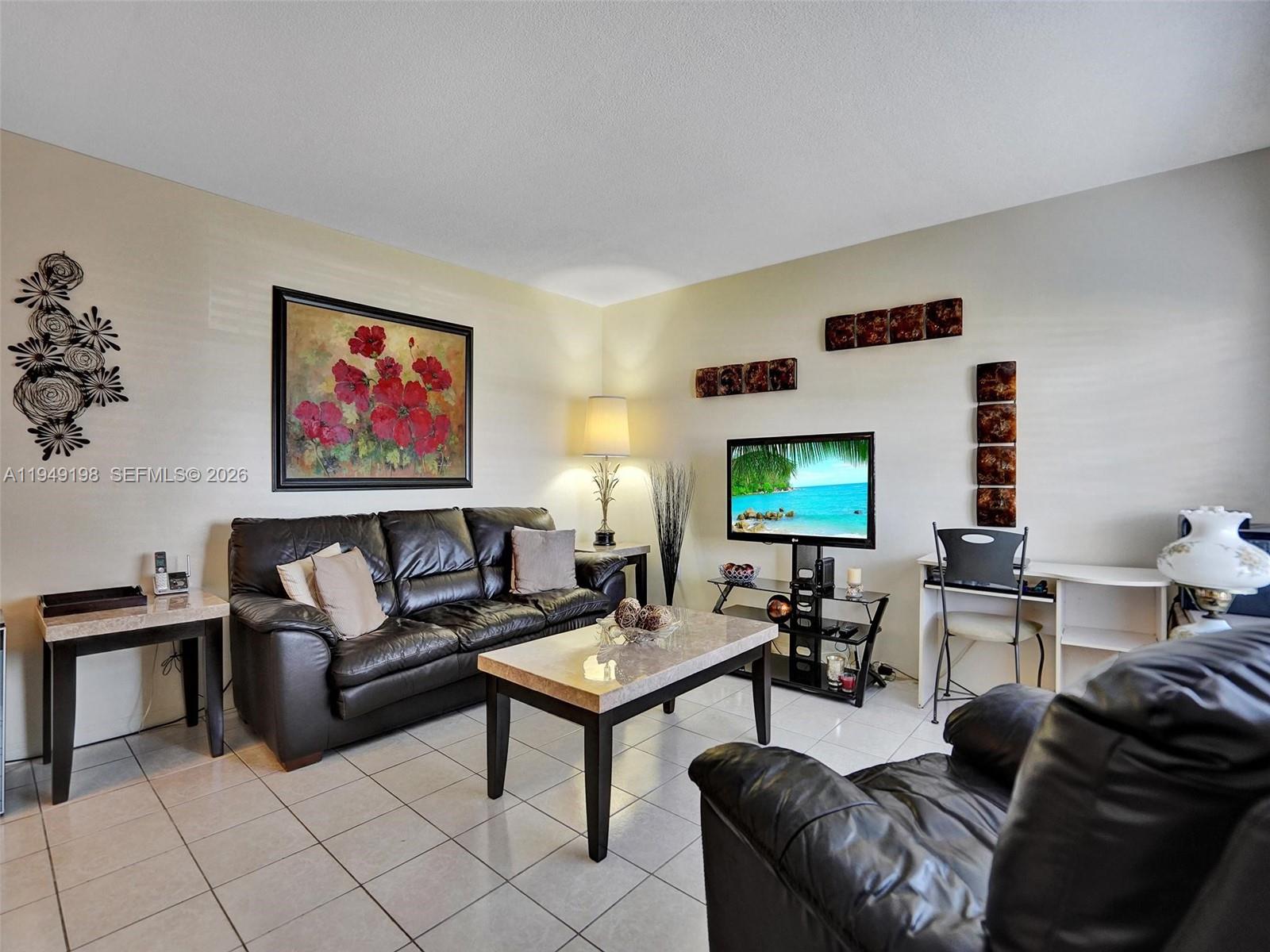 A living room features a dark leather sofa, a coffee table, and a television stand — 16901 NE 13th Ave # 110, Miami FL 33162, MIAMI, FL