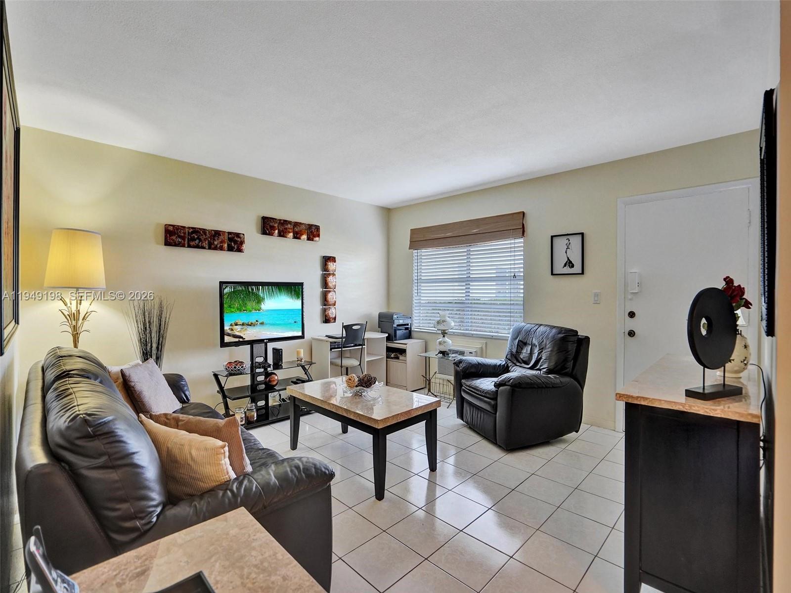A living room features tile flooring, a leather sofa, a recliner, and a television stand — 16901 NE 13th Ave # 110, Miami FL 33162, MIAMI, FL