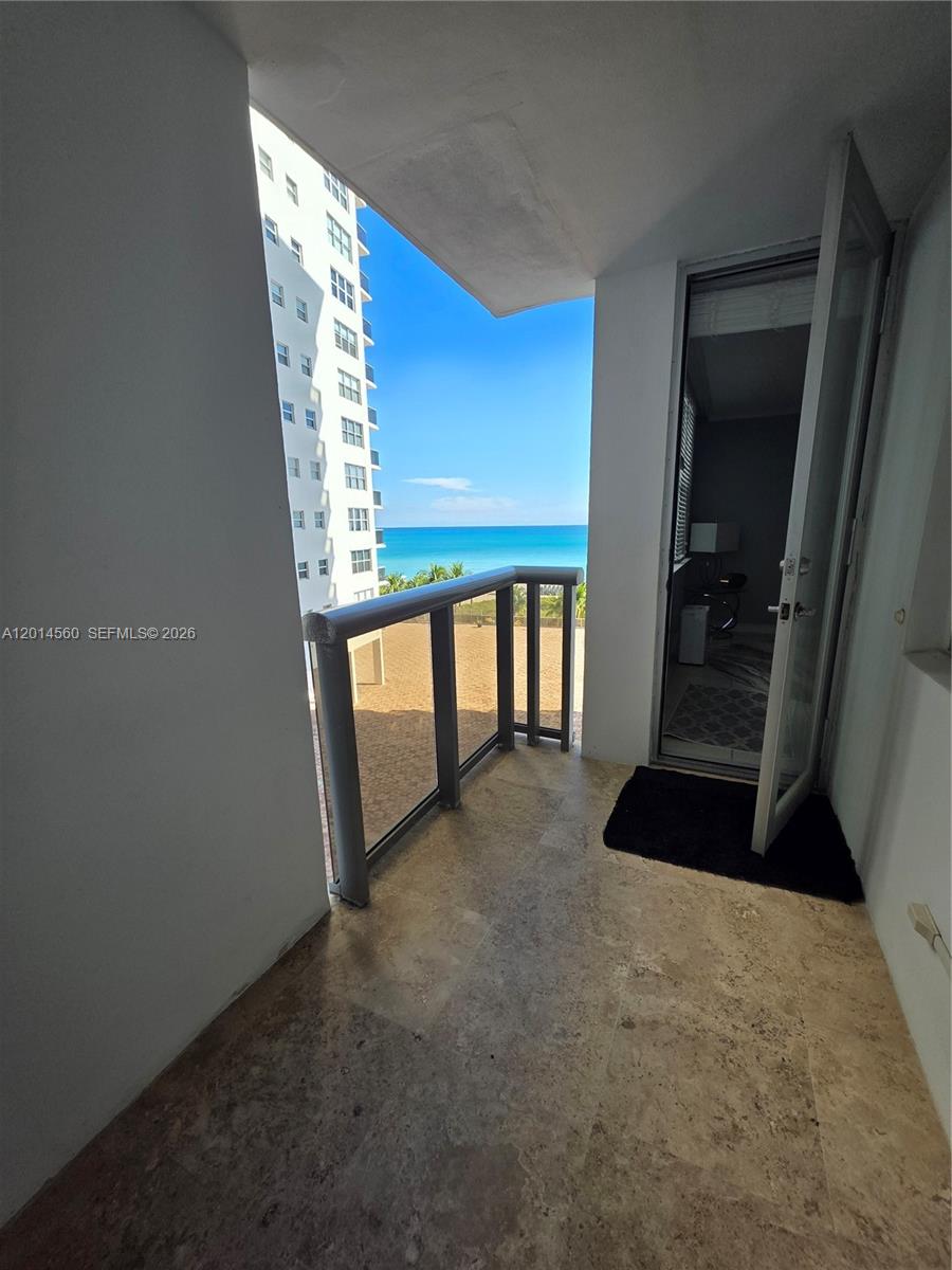 A balcony with stone flooring and a glass railing overlooks the ocean and nearby buildings — 6039 Collins Ave # 621, Miami Beach FL 33140, MIAMI BEACH, FL