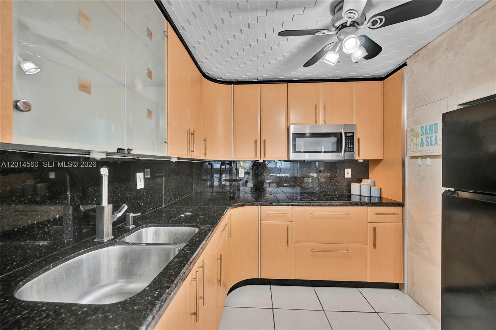 A kitchen features light wood cabinets, black granite countertops, and a ceiling fan — 6039 Collins Ave # 621, Miami Beach FL 33140, MIAMI BEACH, FL