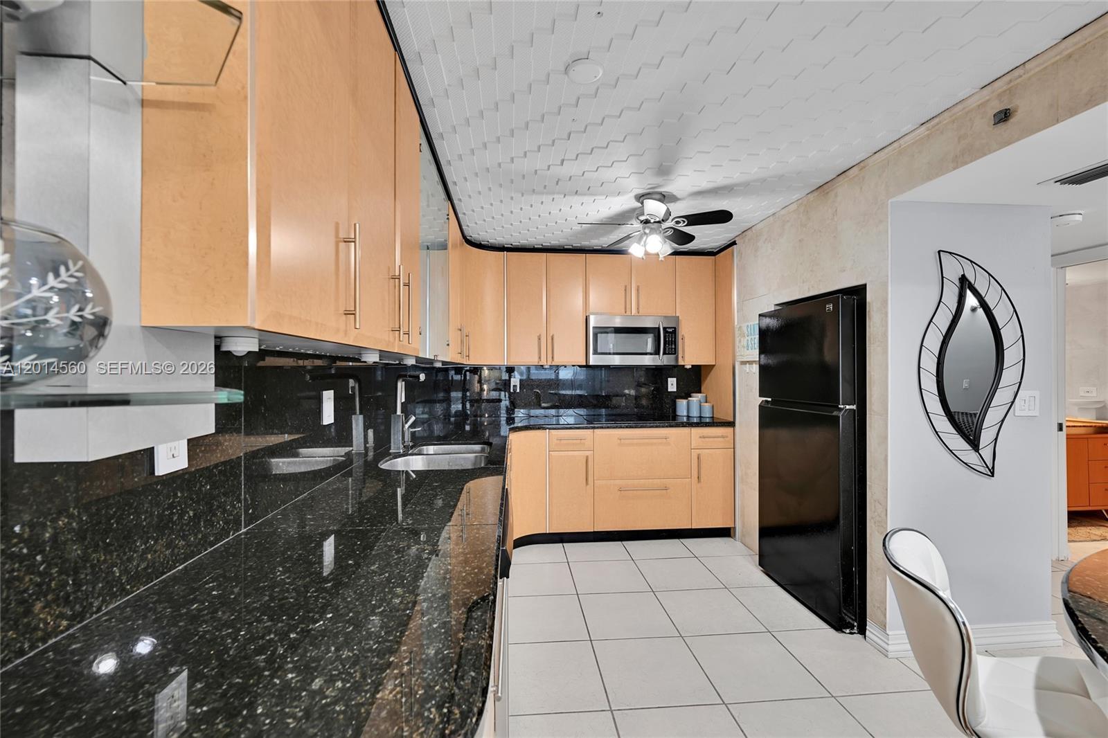 A kitchen features light wood cabinets, black granite countertops, a black refrigerator, and tiled flooring — 6039 Collins Ave # 621, Miami Beach FL 33140, MIAMI BEACH, FL